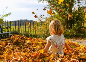 Young girl playing in pile of autumnal leaves