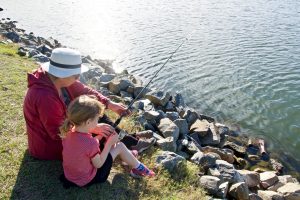Child being taught to fish by grandparent